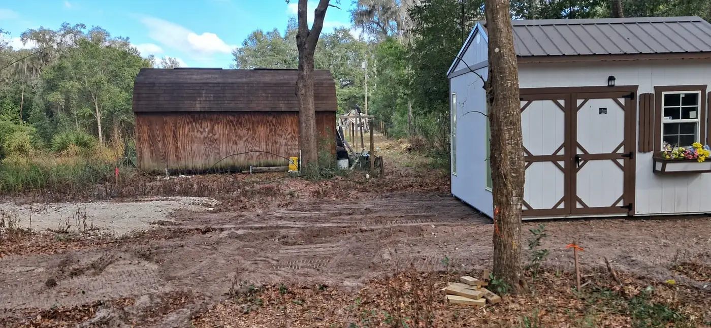 Repositioned white storage shed beside the original building on freshly prepared ground