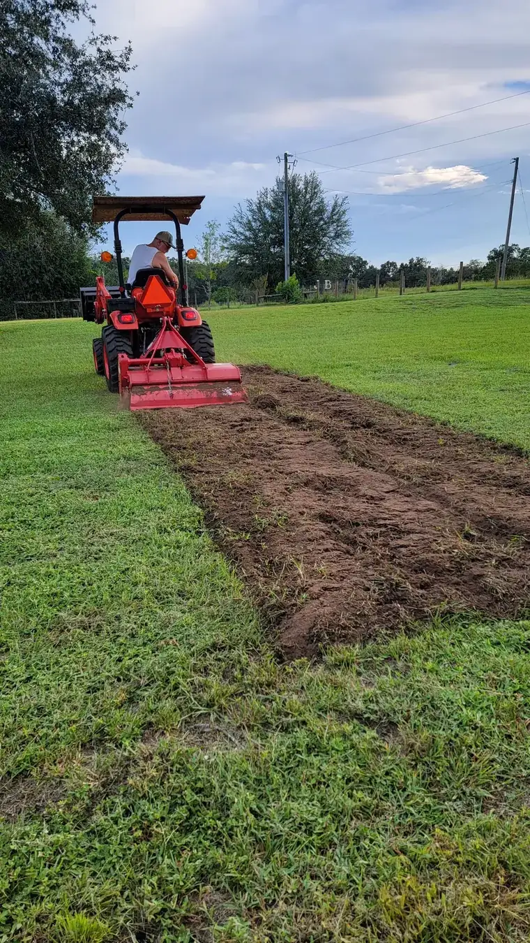 Freshly rototilled soil strip running through green pasture after a pass with the rear tiller