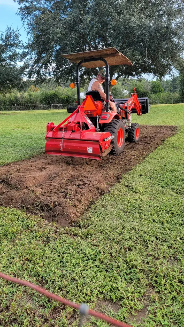 Tractor continuing a rototilling pass, with turned soil on one side and turf on the other